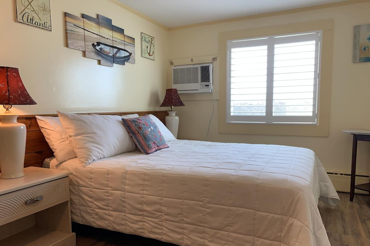 A neatly made bed with a white quilt, a wooden headboard, and a nightstand with a lamp.