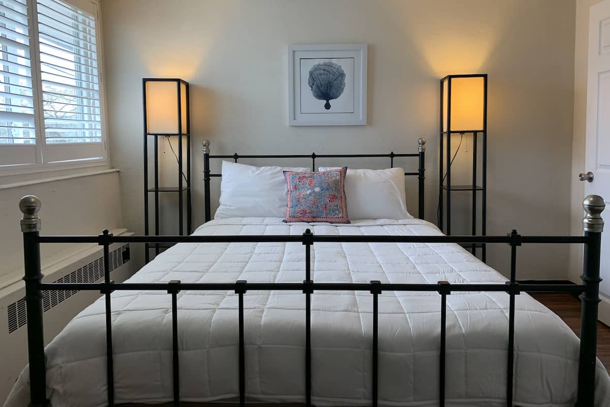 A bed with a white quilt, black metal frame, and two bedside lamps.
