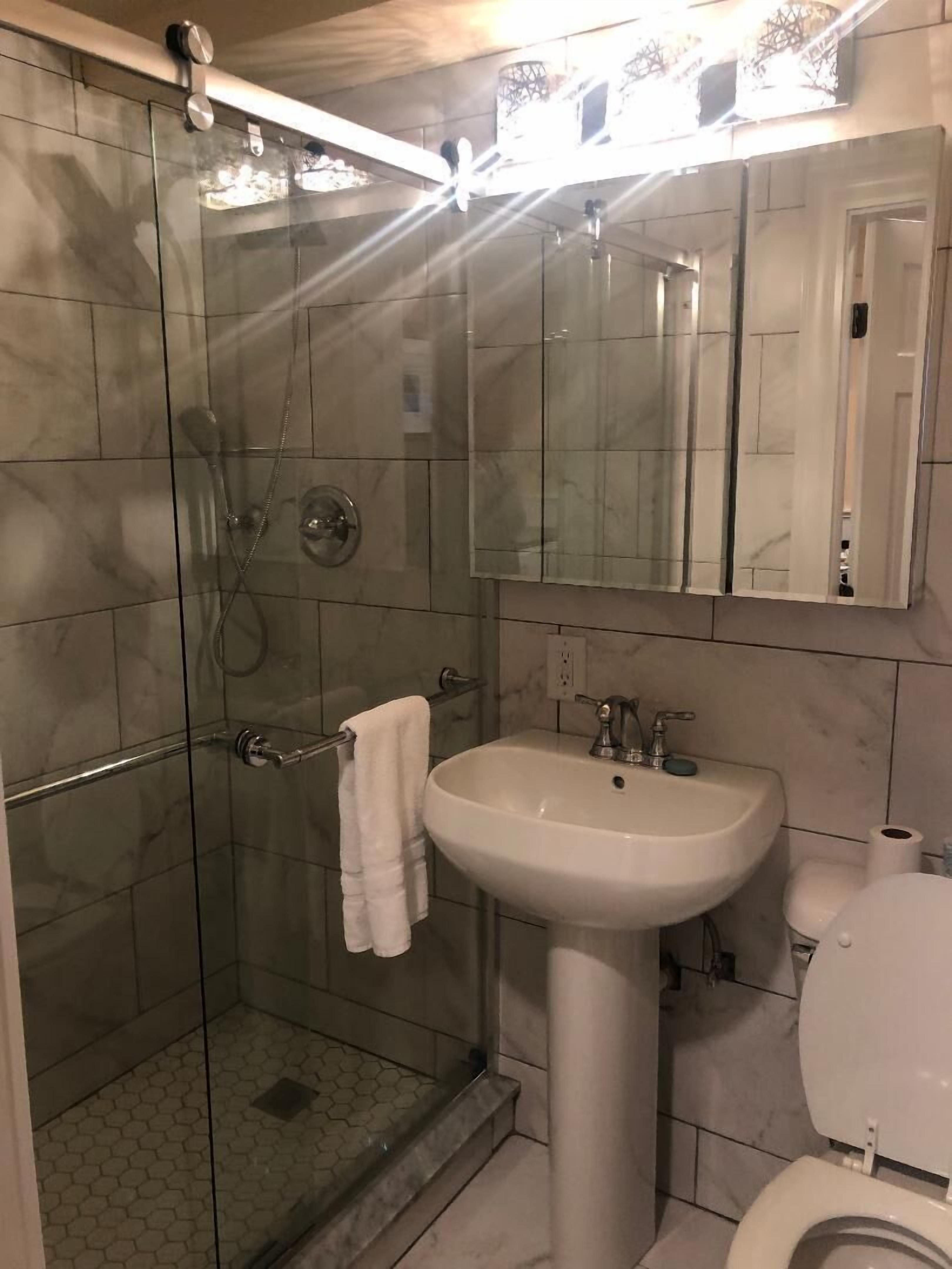 A bathroom with a glass-enclosed shower, a white sink, and a toilet.