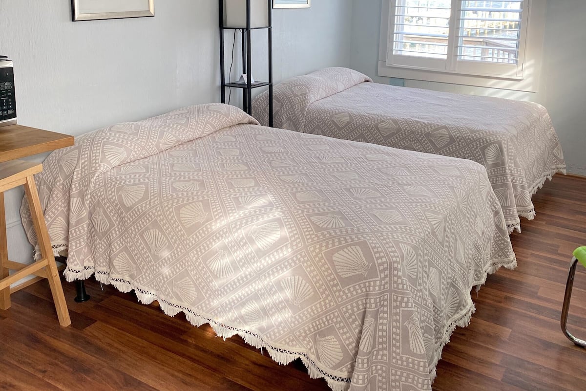 A bedroom with two beds, a desk, and a window with blinds.