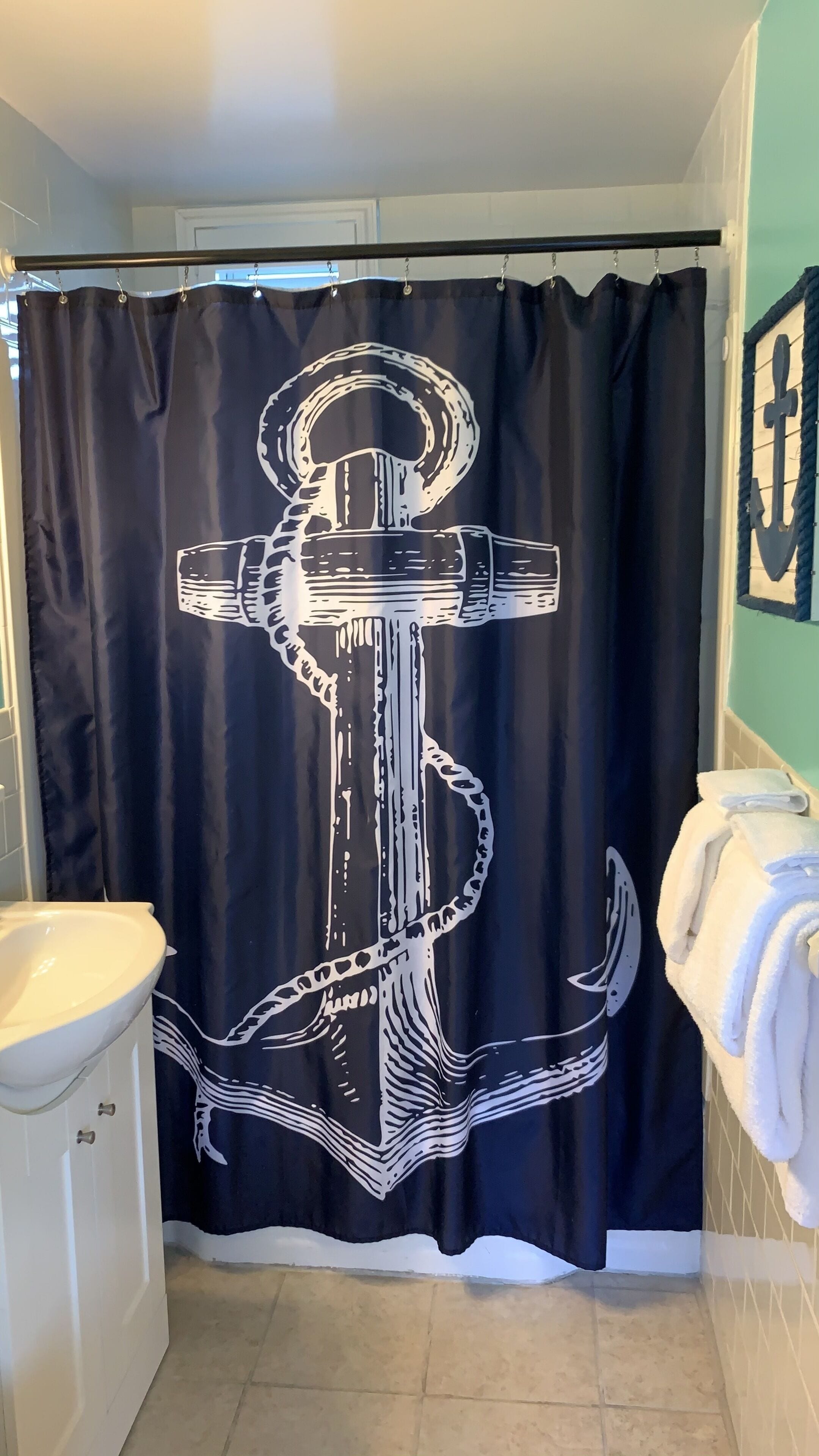 A bathroom with a black shower curtain featuring a white anchor design, a white sink, and a towel rack with folded towels.