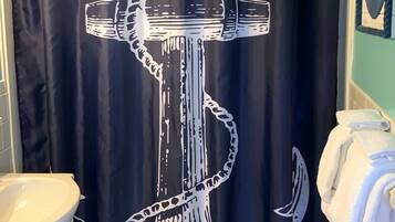 A bathroom with a black shower curtain featuring a white anchor design, a white sink, and a towel rack with folded towels.