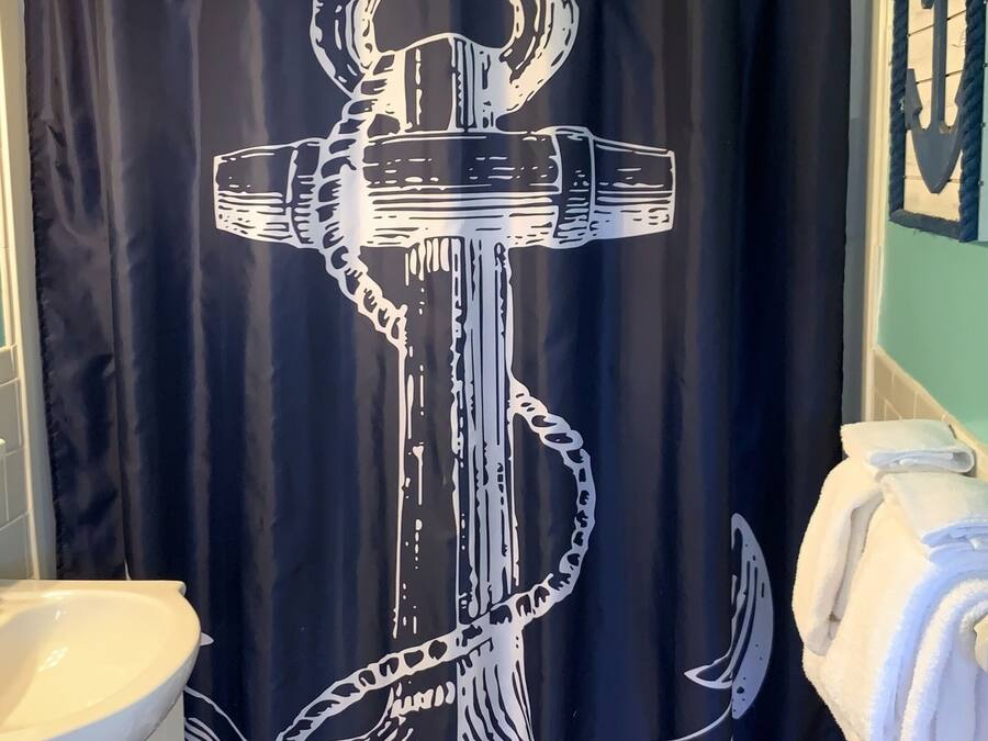 A bathroom with a black shower curtain featuring a white anchor design, a white sink, and a towel rack with folded towels.