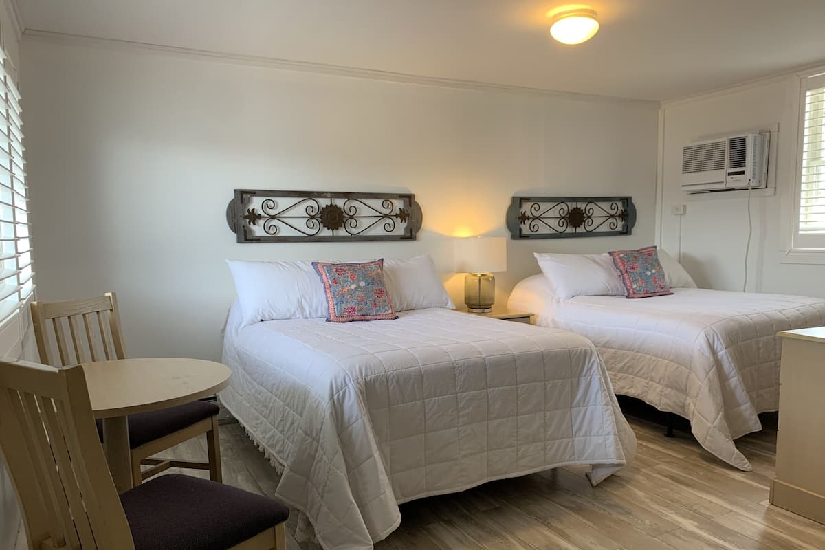 A hotel room with two beds, a wooden chair, a small table, and a ceiling light.