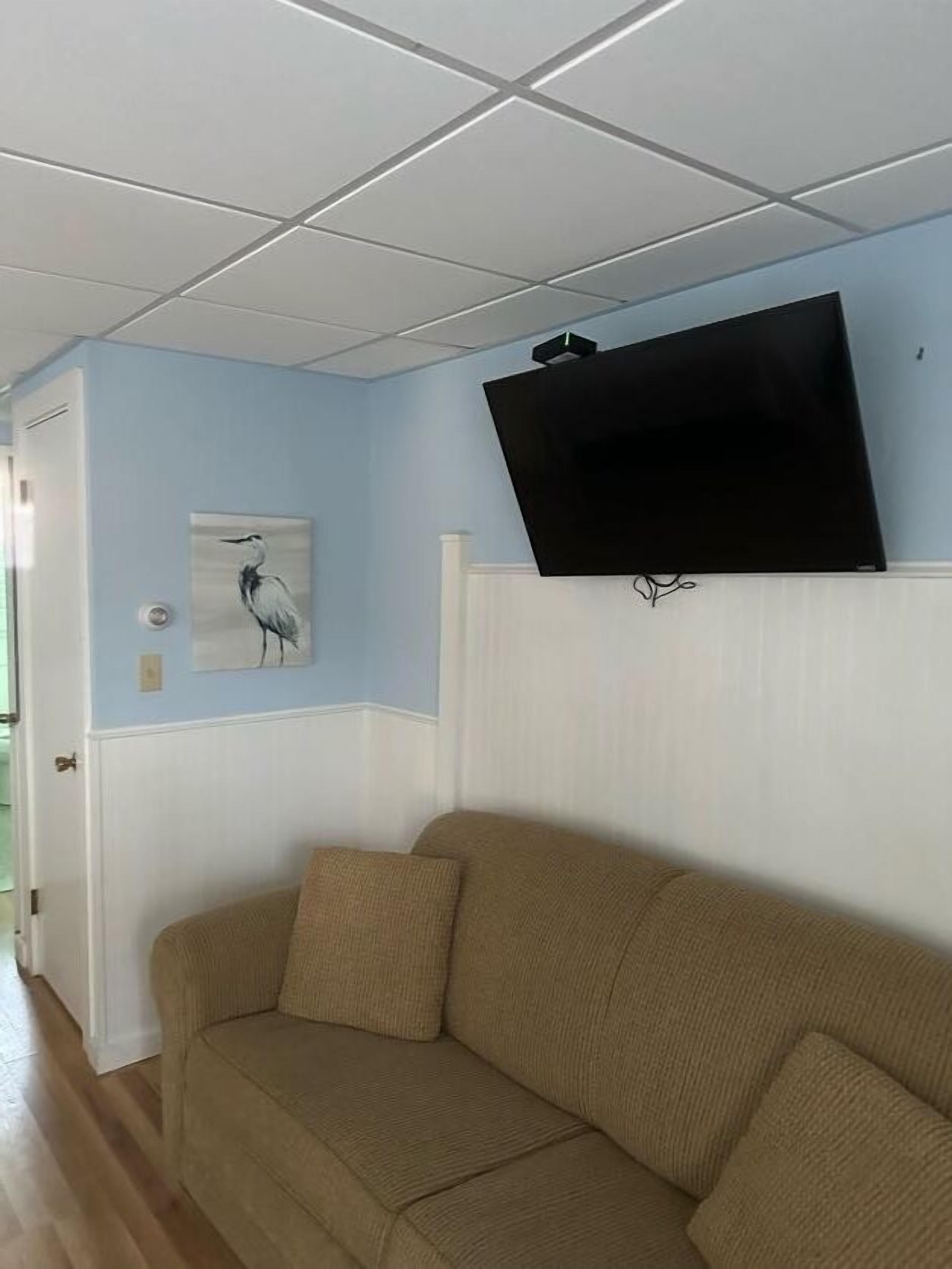 A living room with a beige sofa, a mounted flat-screen TV, and a wall-mounted artwork of a bird.