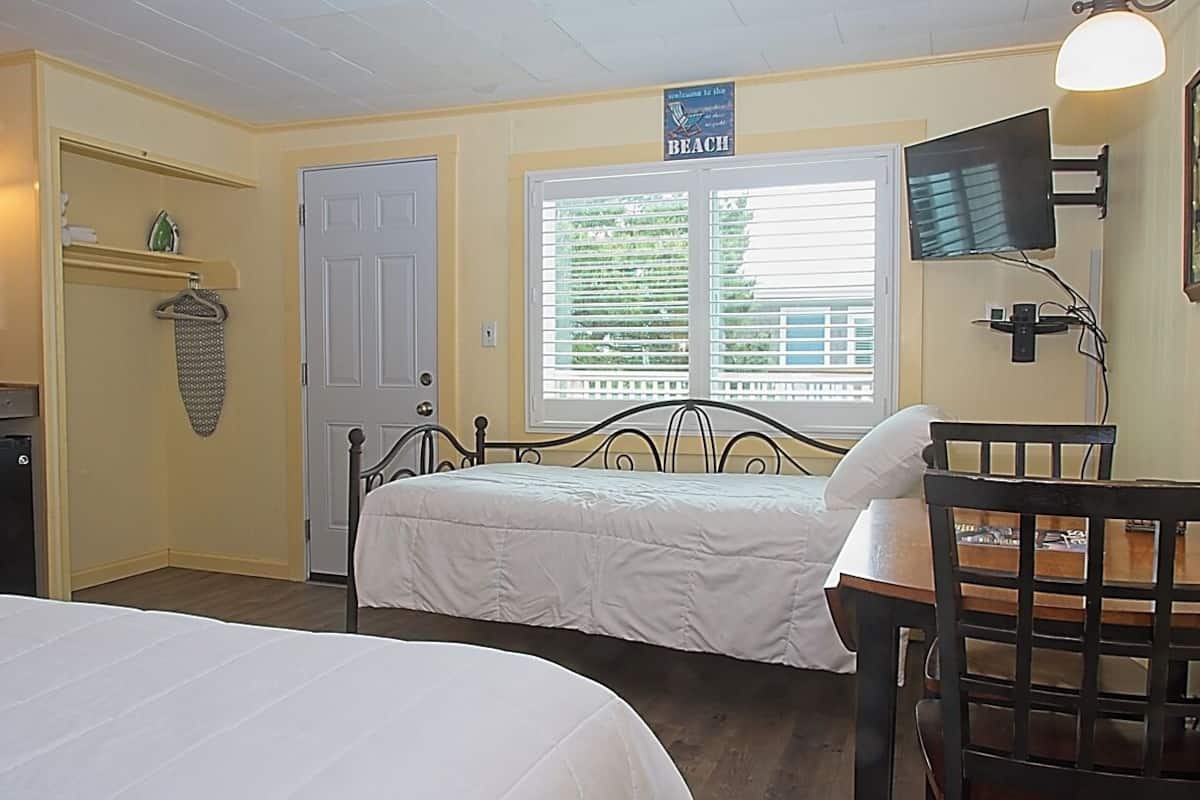 A room with two beds, a television, a chair, and a window with blinds.