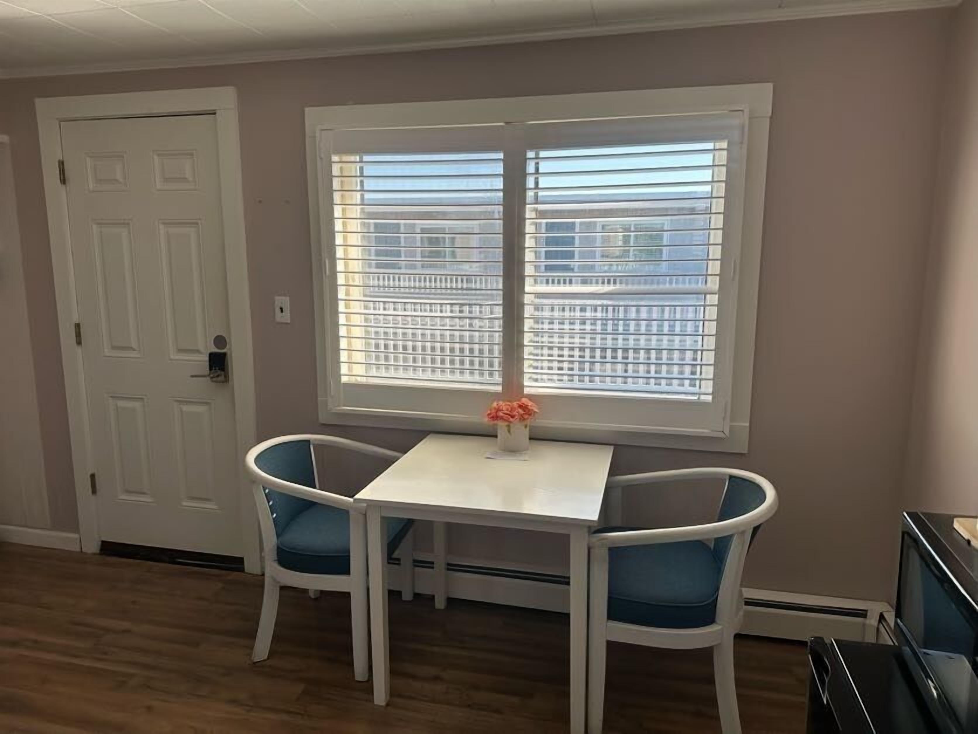 A small room with a white table and two blue chairs, a white door, and a window with blinds.