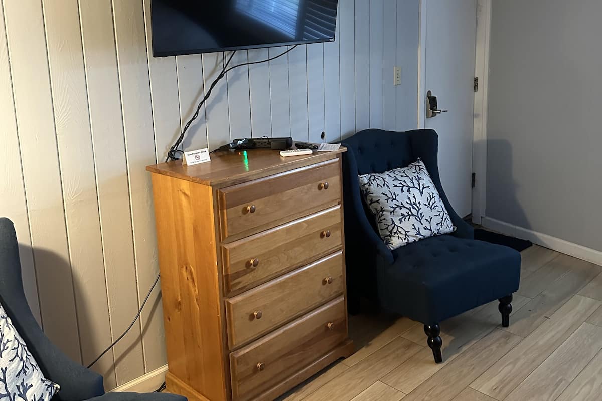 A room with a wooden dresser, a blue armchair, a television mounted on the wall, and a door.