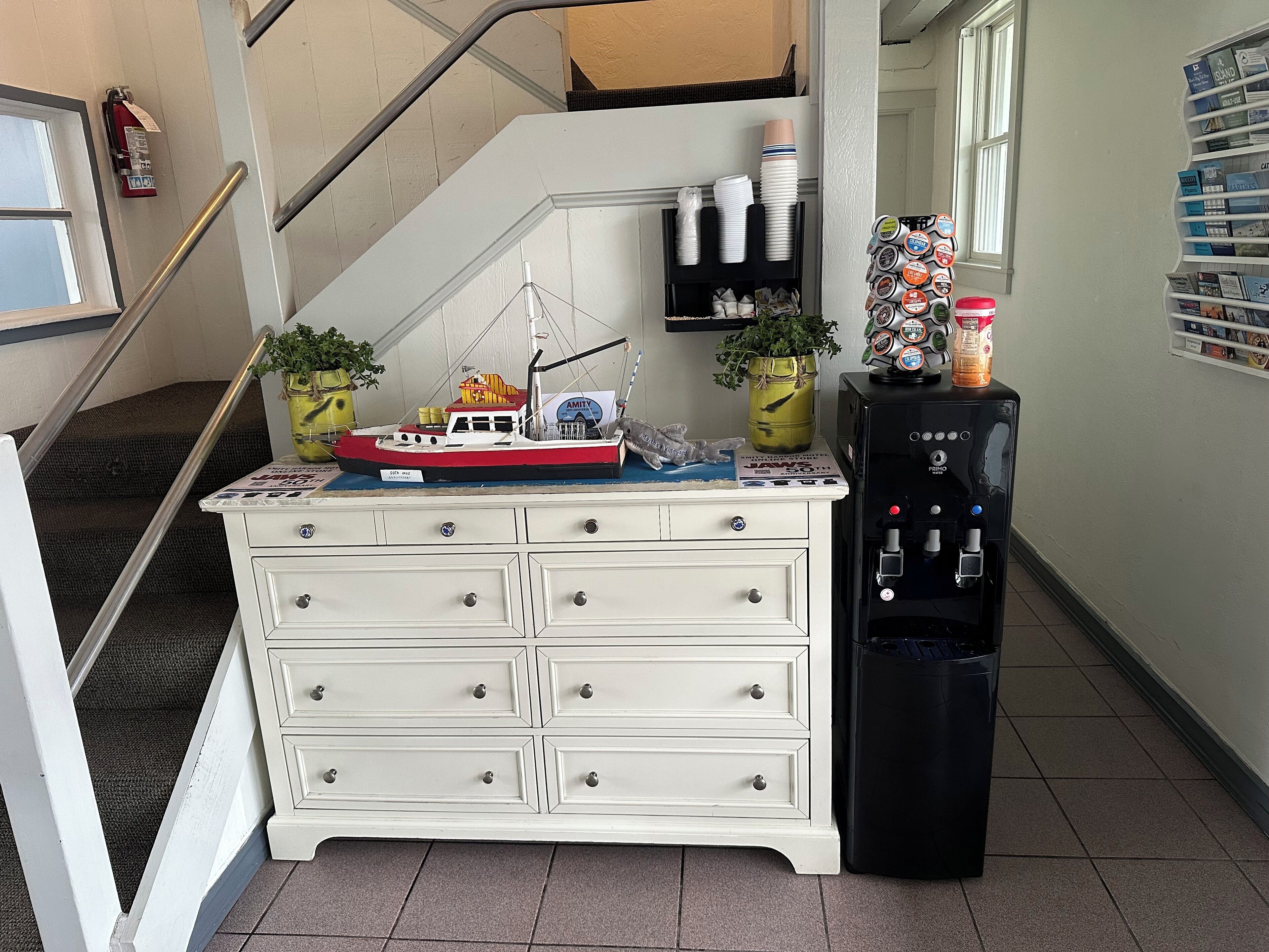 A white dresser with drawers, a small ship model, and a water dispenser in a hallway.