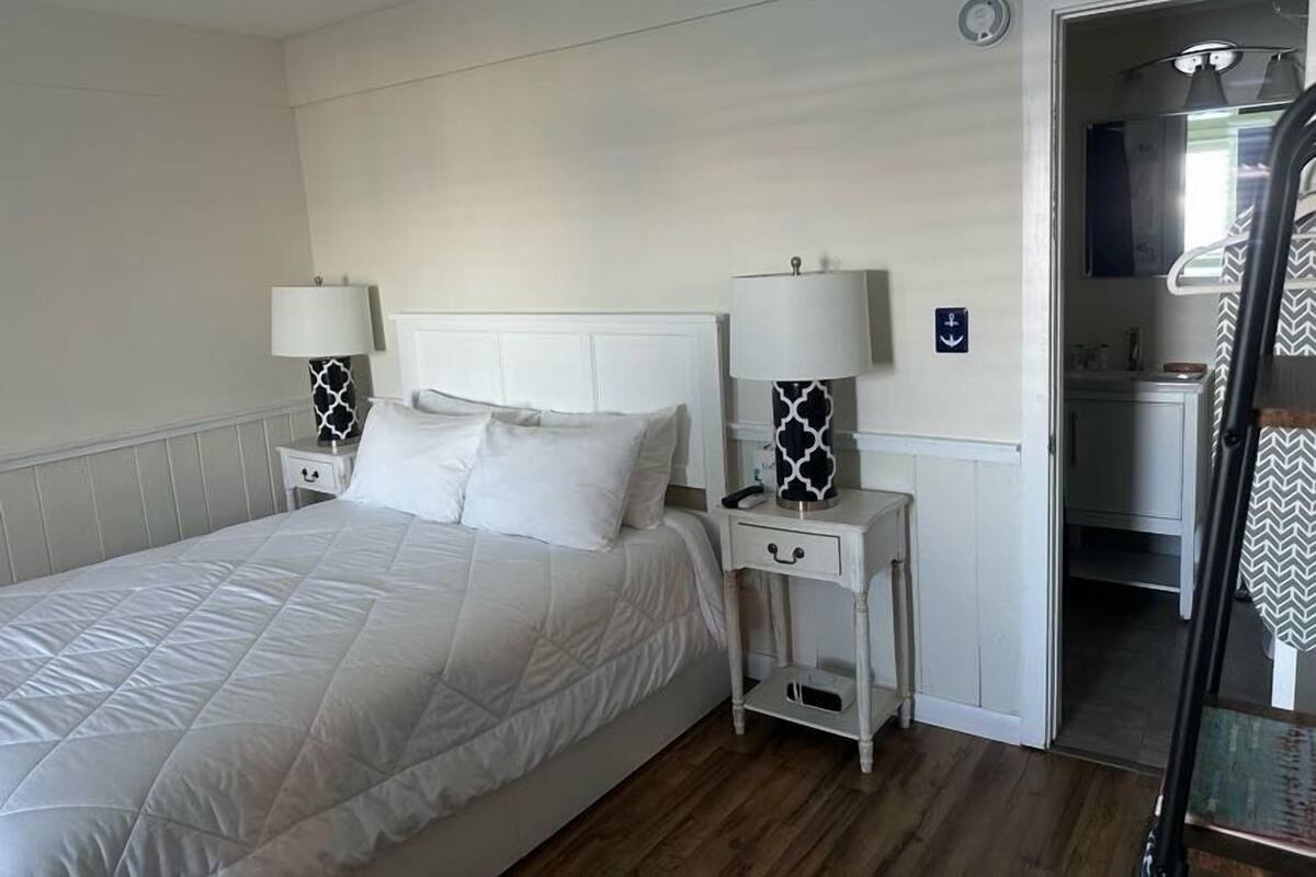 A bedroom with a bed, two bedside tables with lamps, a door leading to a bathroom, and a small cabinet.