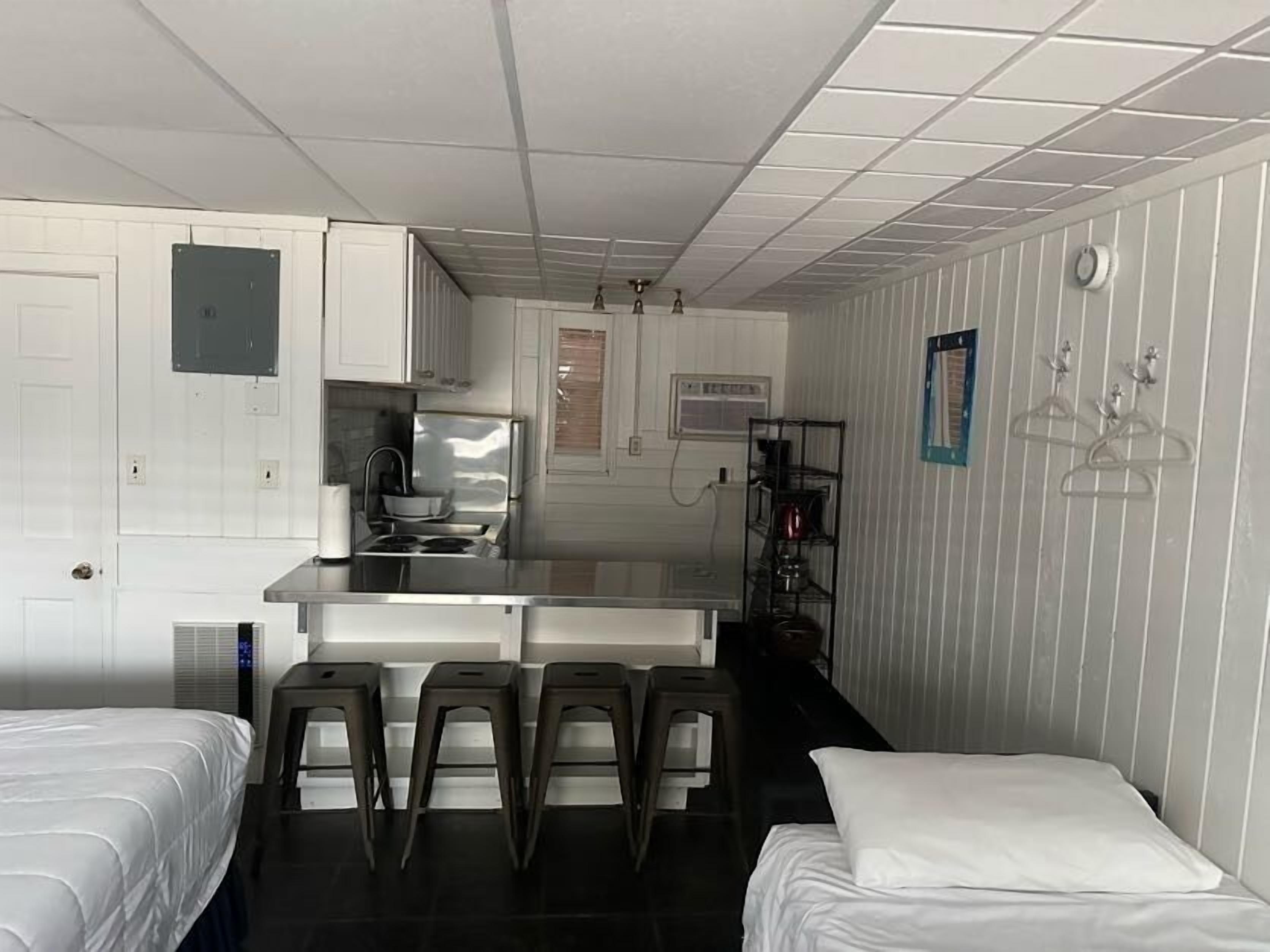 A compact hotel room with a kitchenette, a bed, a small seating area, and a bathroom.