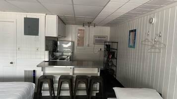 A compact hotel room with a kitchenette, a bed, a small seating area, and a bathroom.