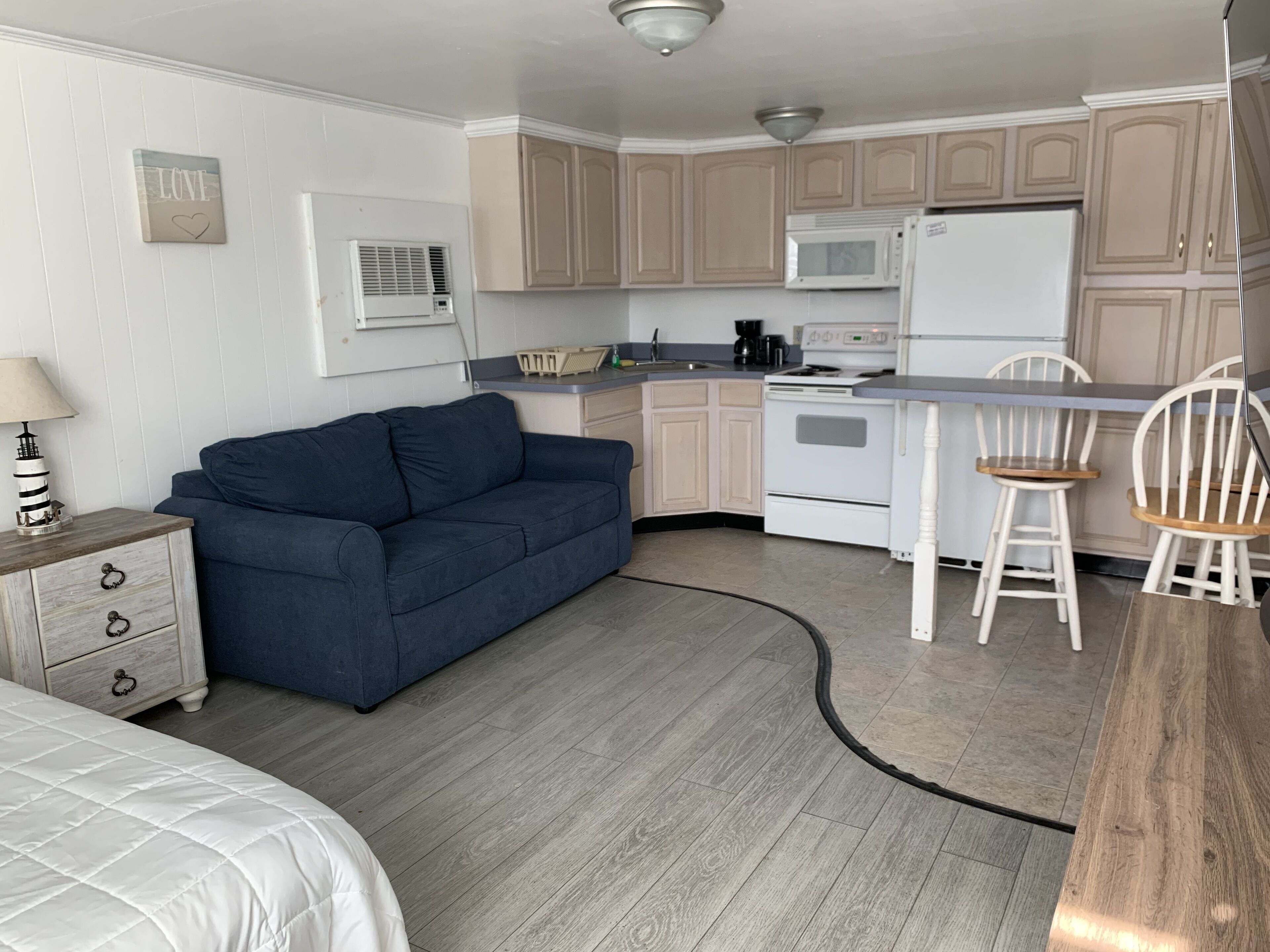 A compact kitchen with a microwave, stove, and white refrigerator. A blue sofa and wooden dining table with two chairs are in the living area.