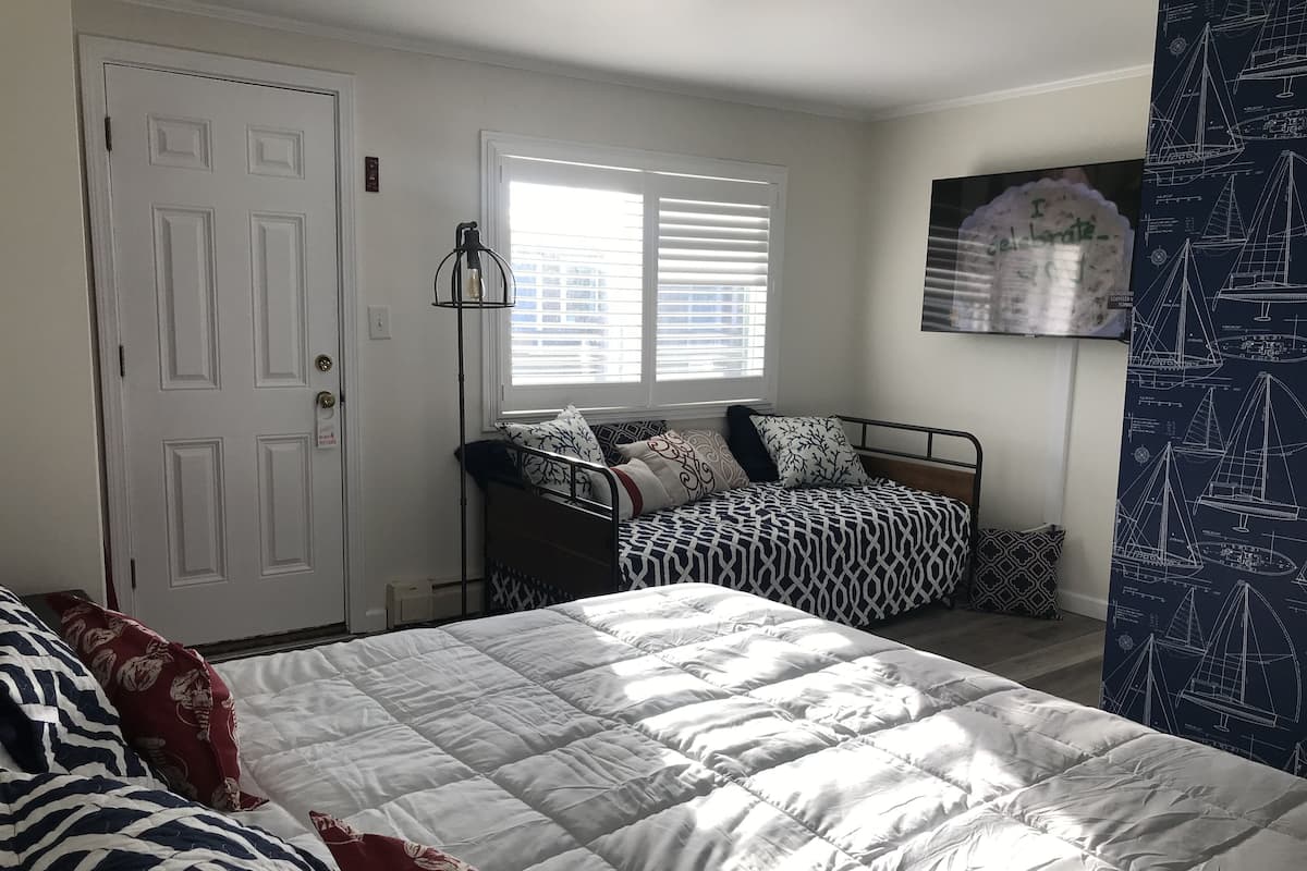 A bedroom with a bed, a window with blinds, a door, and a wall with a nautical-themed poster.