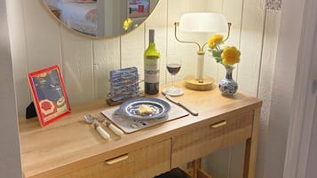 A wooden desk with a mirror, a framed picture, a wine bottle, a candle, and a vase with flowers.