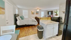 Un espacio habitable compacto con kitchenette, una cama con cabecera, una mesa de comedor y un cubo de basura.