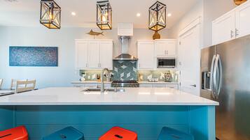 A modern kitchen with a central island, bar stools, and pendant lighting.
