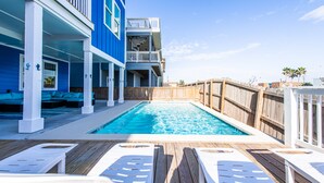 Un espace piscine avec des chaises longues en bois, une piscine et un bâtiment doté de balcons.