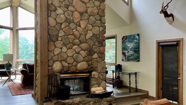 A spacious living room with a stone fireplace, wooden chairs, and a large window offering a view of the outdoors. - Mt. Crested Butte Full House, 3 Bedroom/3.5 Bath+Loft, Hot Tub, Shuttle  to Ski (Crested Butte)
