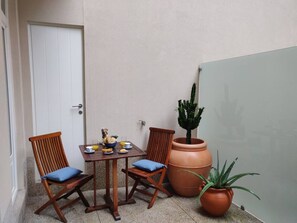 Un piccolo patio con un tavolo, due sedie, una pianta in vaso e una porta.