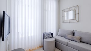 Een moderne woonkamer met een grijze bank, twee gestreepte kussens, een rond voetenbankje en een spiegel aan de muur.