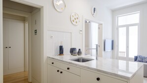 Een moderne keuken met witte kastjes, een marmeren aanrechtblad en een inbouwspoelbak. Er hangen decoratieve borden aan de muur en boven de spoelbak is een televisie bevestigd.