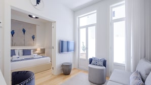 Een moderne woonkamer met een bank, een stoel, een televisie en een bed met een blauw-witte spreideken.