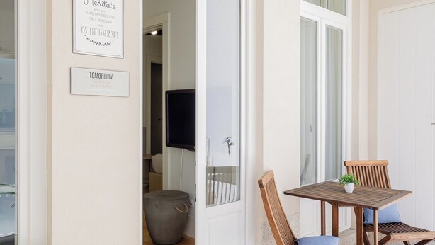 Een moderne kamer met een witte bank, een houten tafel met stoelen en een kleine potplant. Twee borden hangen aan de muur, waarvan er een 'Meditate' en de andere 'Tomorrow' zegt.