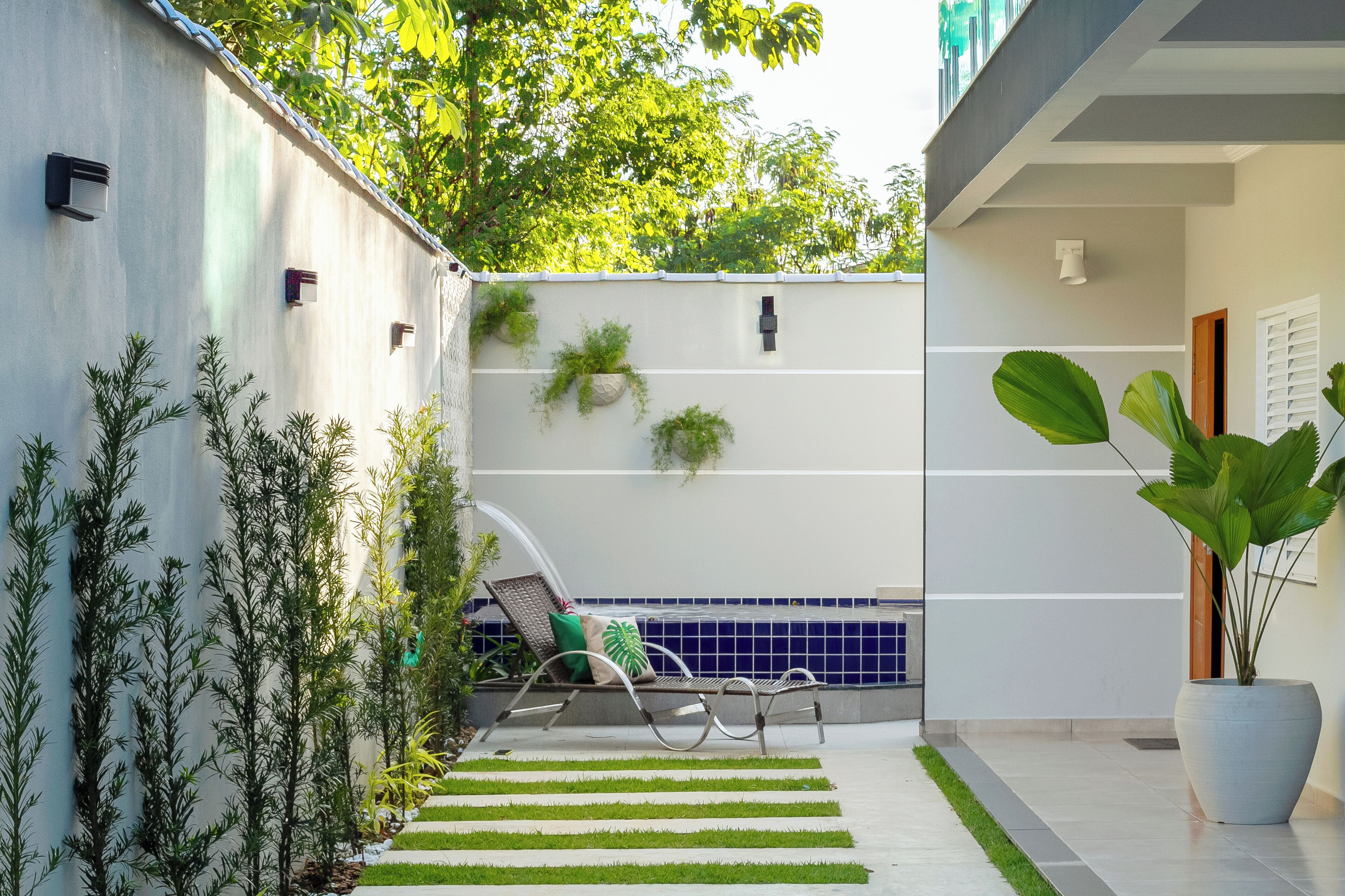 A modern outdoor patio with a lounge chair, potted plants, and a tiled floor.
