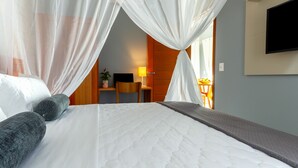 A hotel room with a bed, a desk, a chair, a TV, and a window with curtains. - Calamar Flats Paraty (Paraty)