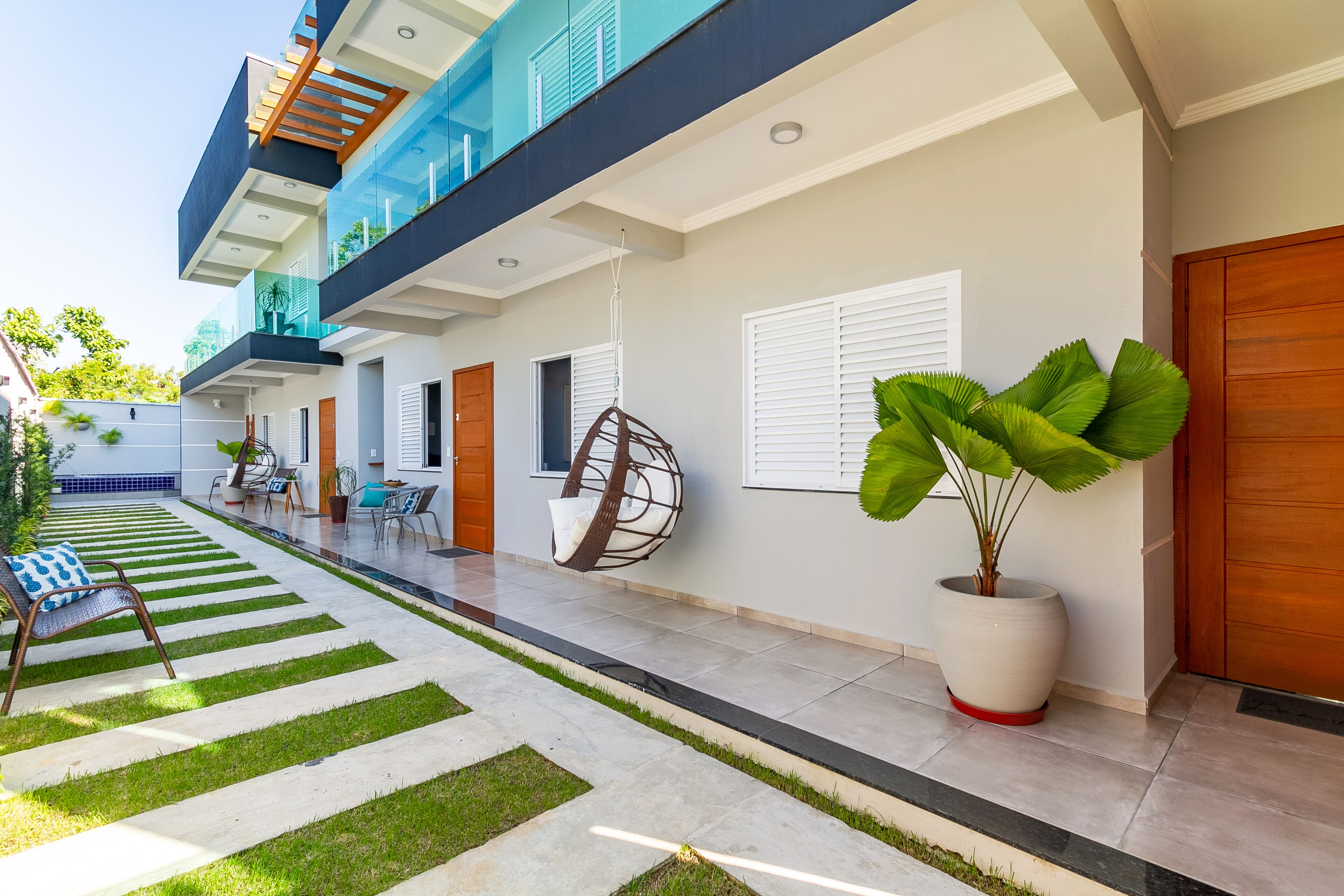 Une maison moderne à deux étages, dotée d’un balcon, d’un fauteuil suspendu et d’une plante en pot.