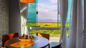 A dining area with a table, chairs, a bowl of pinecones, and a view of a beach through sheer curtains. - Calamar Flats Paraty (Paraty)