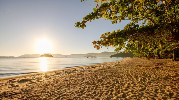 A beach with a clear sky and the sun setting or rising over the water. - Calamar Flats Paraty (Paraty)