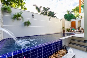Una piscina con borde de azulejos azules, una fuente de agua y escalones que bajan a la piscina.
