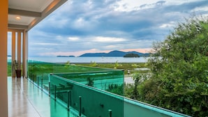 A balcony with a glass railing overlooking a body of water and greenery. - Calamar Flats Paraty (Paraty)