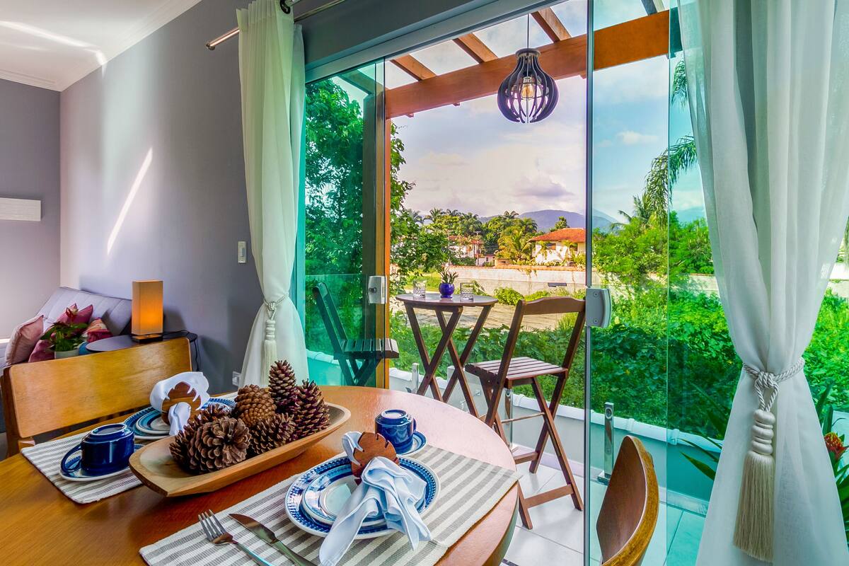 Uma área de refeições com uma mesa posta para dois, com pinhas, um bule azul e uma cadeira de madeira.