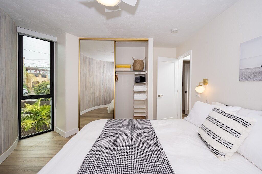 Een slaapkamer met een groot bed, een kast met planken, een raam met uitzicht en een nachtkastje met een lamp.