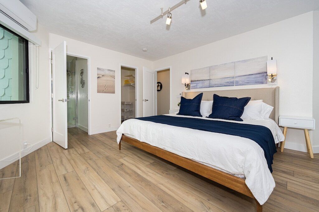 Ein Schlafzimmer mit Bett, Holzboden, wei ßer Wand, einem Gemälde und einem Nachttisch.