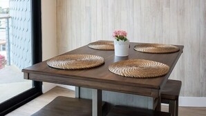 Ein Essbereich mit einem modernen Kronleuchter, einem Holztisch, gewebten Platzsets und einer Vase mit Blumen.