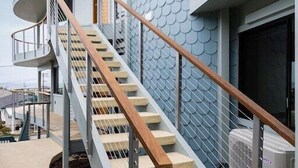 Ein modernes Gebäude mit einem einzigartigen, schuppenartigen Außendesign, einer Holztreppe mit Metallgeländern und einem klaren Himmel im Hintergrund.