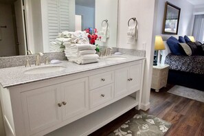 A bathroom with a double sink vanity, a large mirror, and a stack of white towels. - Renovated Ocean View Condo - Great Beach Walks & Bike Rides (St. Augustine)