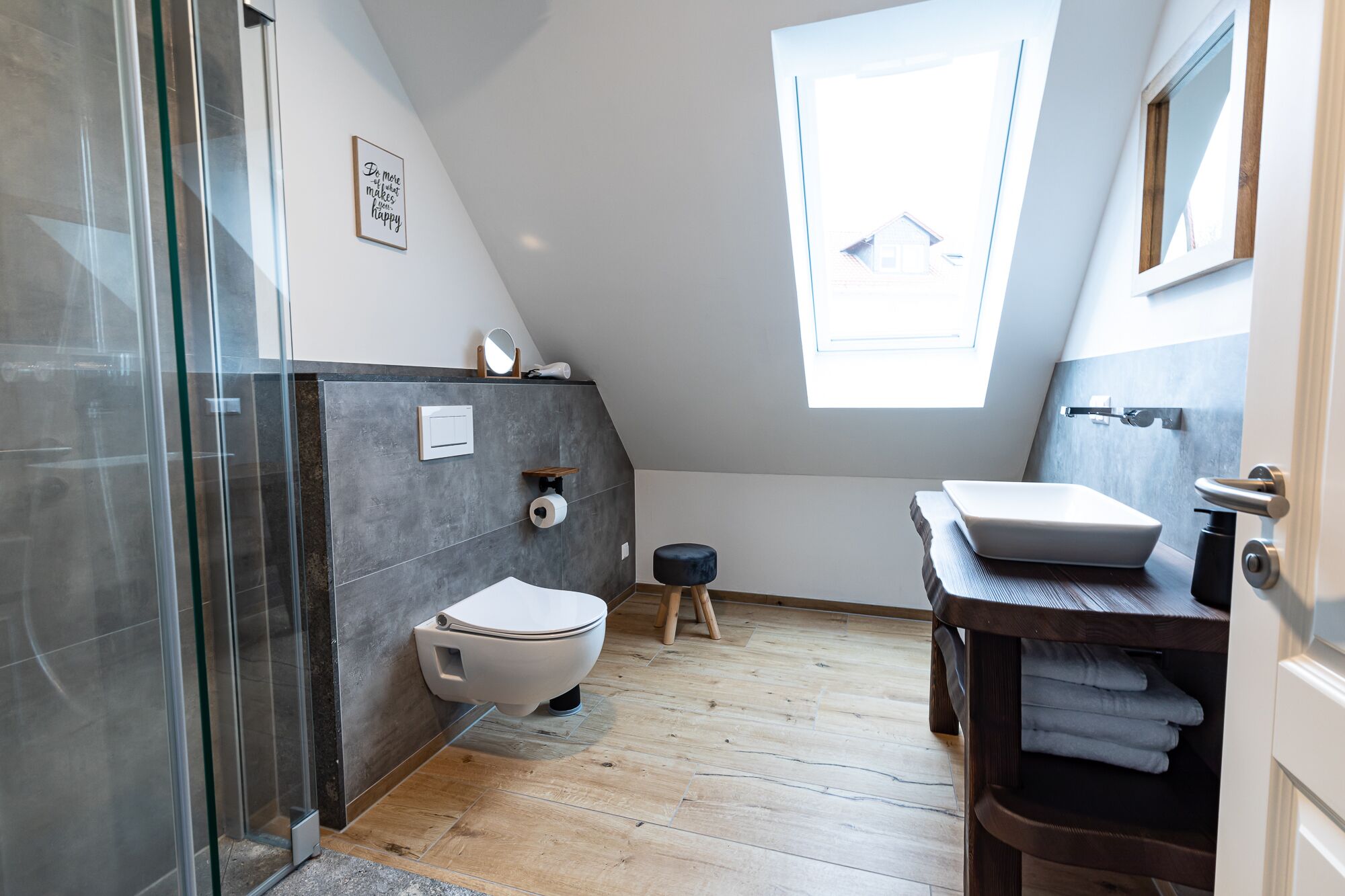 A modern bathroom with a glass shower enclosure, a toilet, a sink, and a small stool.