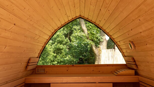 A wooden interior with a sloped ceiling and a window overlooking a green area. - Vacation home Heuliebe, barbecue hut, whirlpool, outdoor sauna (Herbstein)