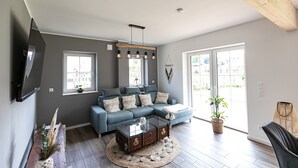 A modern living room with a sectional sofa, a glass coffee table, and a large window providing natural light. - Vacation home Heuliebe, barbecue hut, whirlpool, outdoor sauna (Herbstein)