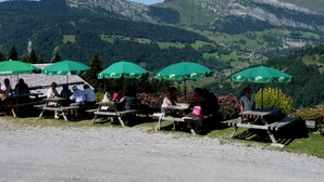 Un'area salotto all'aperto suggestiva, con tavoli da picnic e ombrelloni verdi, con vista su un paesaggio montuoso.