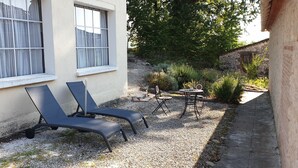 En terrasse med to liggestole, et lille bord og en have med planter samt en stenvæg.