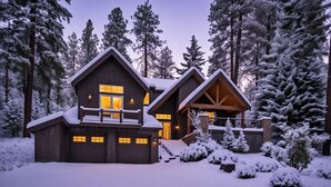 A large, two-story log cabin with a covered porch and a garage, surrounded by snow-covered trees.
