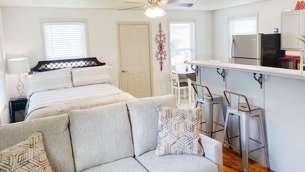 A compact, well-lit room with a bed, a sofa, a dining area with a bar, and a kitchenette. - Furnished Red Studio central location near restaurants, Lake & shopping (Hot Springs)