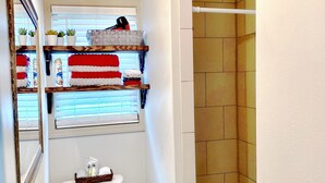 A bathroom with a toilet, sink, and shower. There are shelves above the toilet with towels and toiletries. - Furnished Red Studio central location near restaurants, Lake & shopping (Hot Springs)