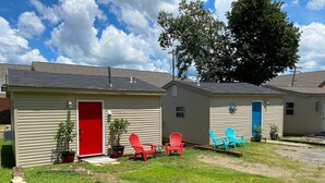 A row of single-story buildings with a red door, blue door, and a small porch area with outdoor seating. - Furnished Red Studio central location near restaurants, Lake & shopping (Hot Springs)